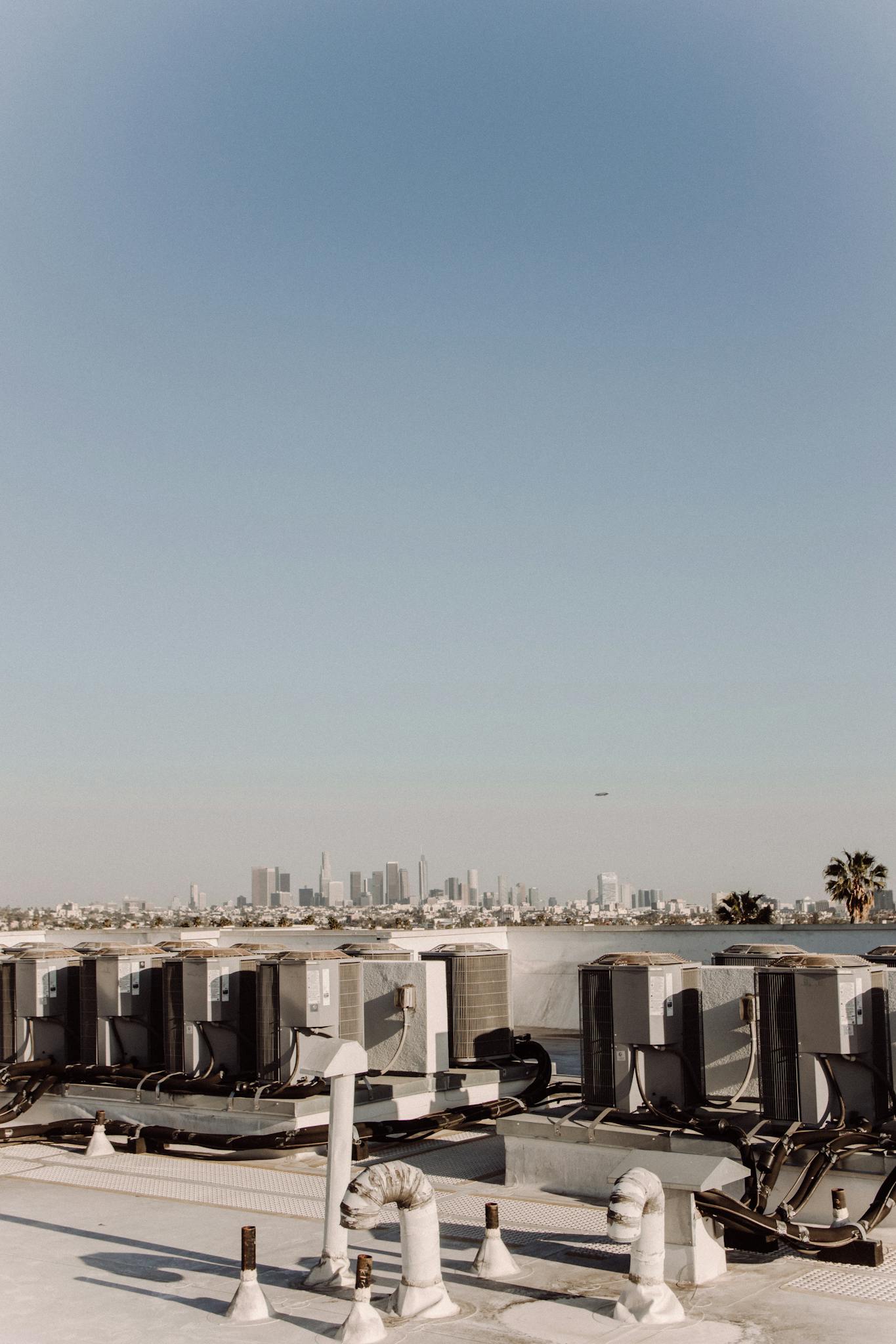 Rooftop HVAC units facing a distant city skyline under a clear blue sky.